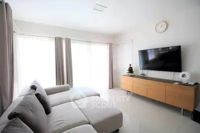 Spacious modern living room with large sofa and wall-mounted TV, perfect for relaxation.