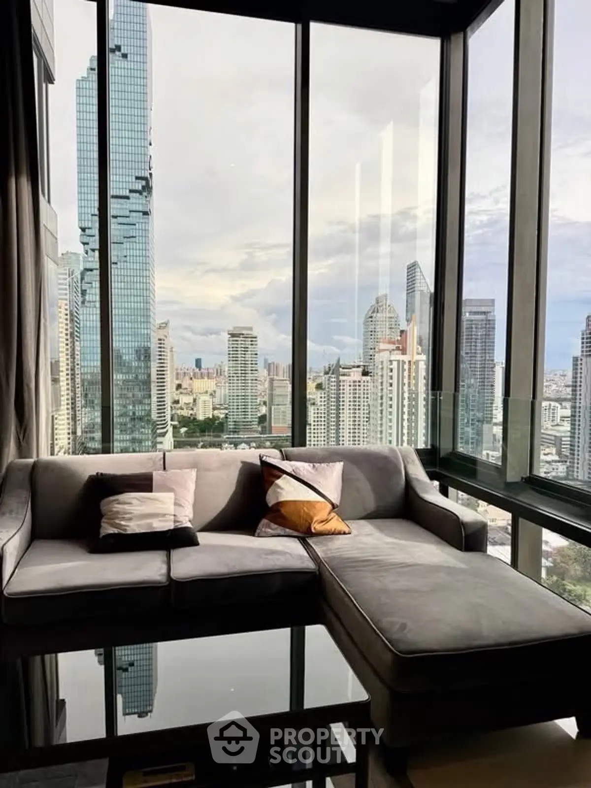 Luxurious living room with panoramic city view from high-rise apartment, featuring modern sofa and floor-to-ceiling windows.