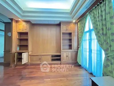 Spacious living room with elegant wooden cabinetry and large window with green curtains.
