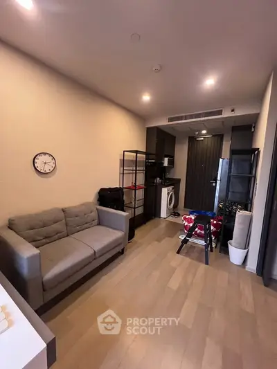 Modern living room with cozy sofa and compact kitchen area, featuring a washing machine and stylish decor.