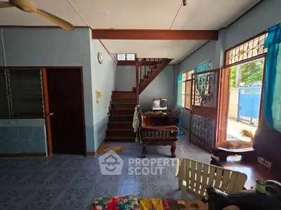 Charming living room with staircase and open entrance, featuring tiled flooring and natural light.