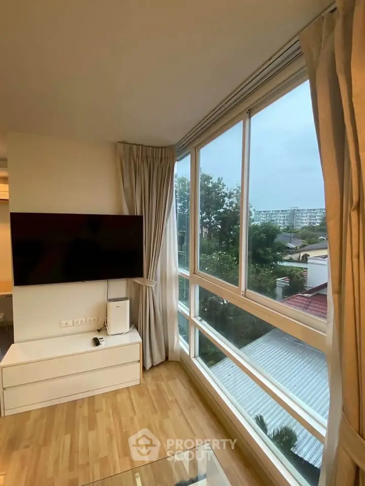 Bright living room with large windows offering a stunning view, modern TV setup, and elegant wooden flooring.