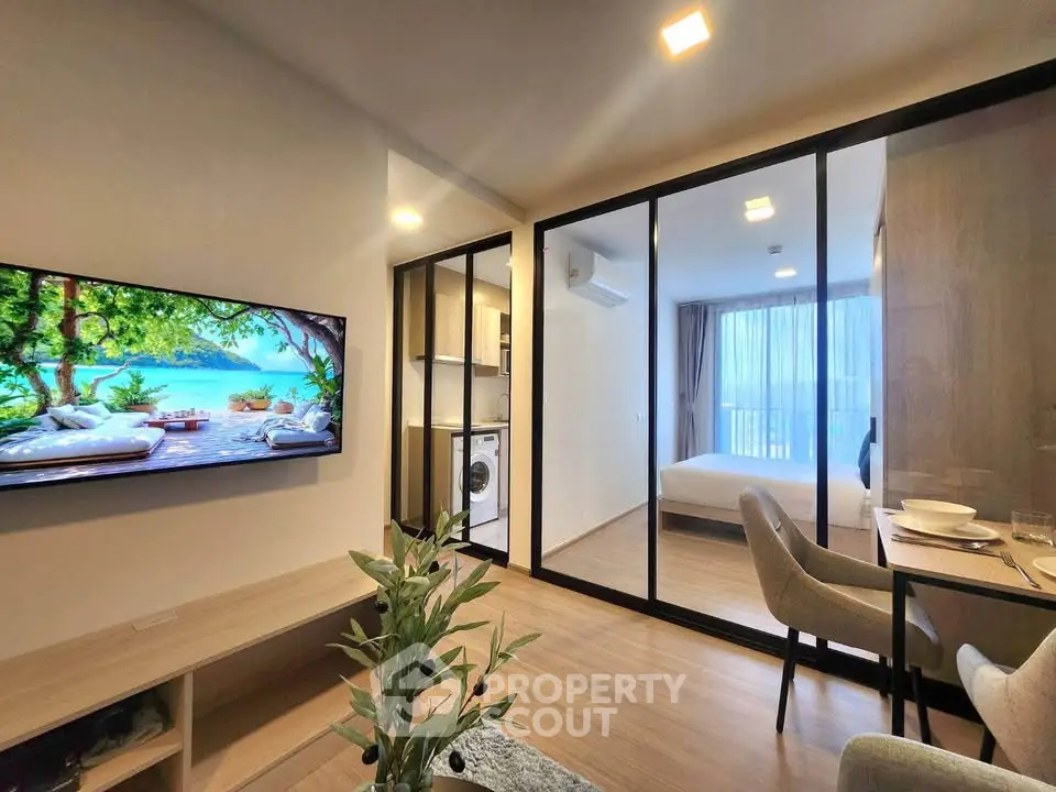Modern open-plan living room with glass partition, cozy bedroom, and stylish kitchen area.