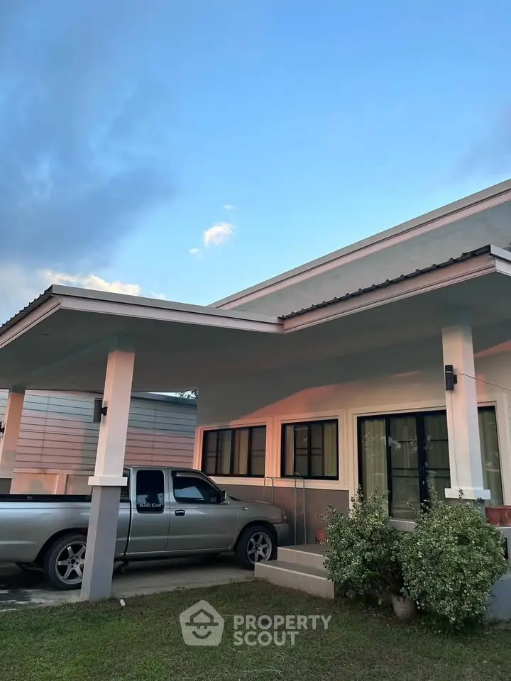 Modern single-story house with carport and lush greenery at sunset.