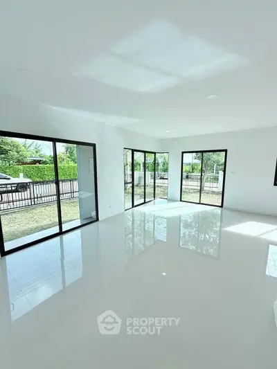Spacious modern living room with large windows and glossy floors, offering abundant natural light and garden views.
