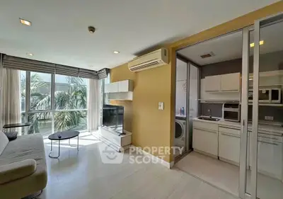 Modern living room with natural light and adjacent kitchen in open layout apartment.