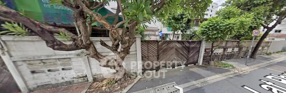 Charming street view with lush greenery and rustic wooden gate, perfect for urban living.