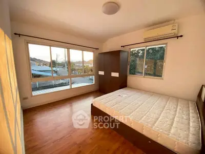 Spacious bedroom with large windows and wooden flooring, offering natural light and scenic views.