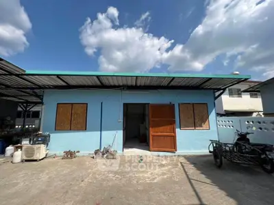 Charming single-story blue house with a metal roof under a clear sky, ideal for cozy living.