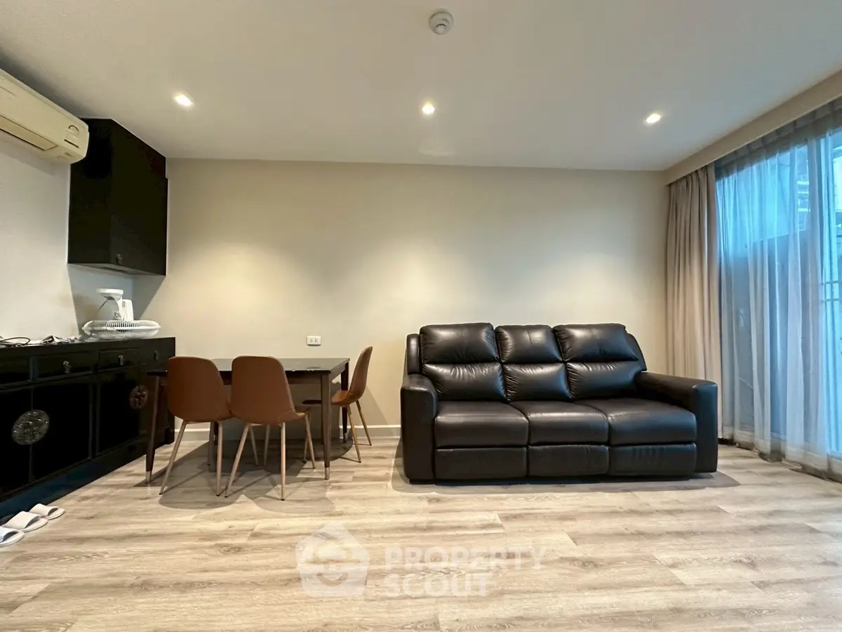Modern living room with black leather sofa and dining area, featuring sleek flooring and ambient lighting.
