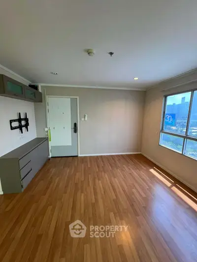 Spacious empty room with wooden flooring and large window offering city view.