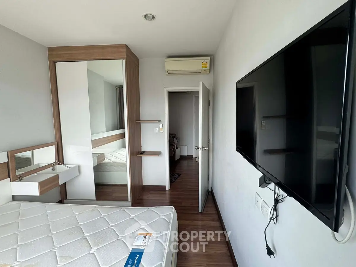 Modern bedroom with wall-mounted TV and built-in wardrobe in stylish apartment.