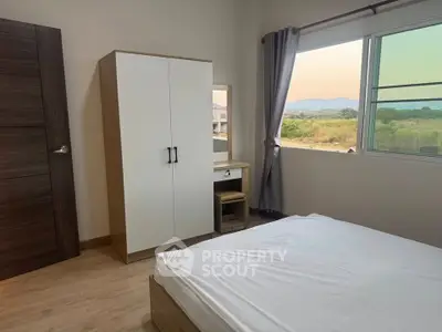 Bright bedroom with large window and scenic view, featuring a wardrobe and dressing table.