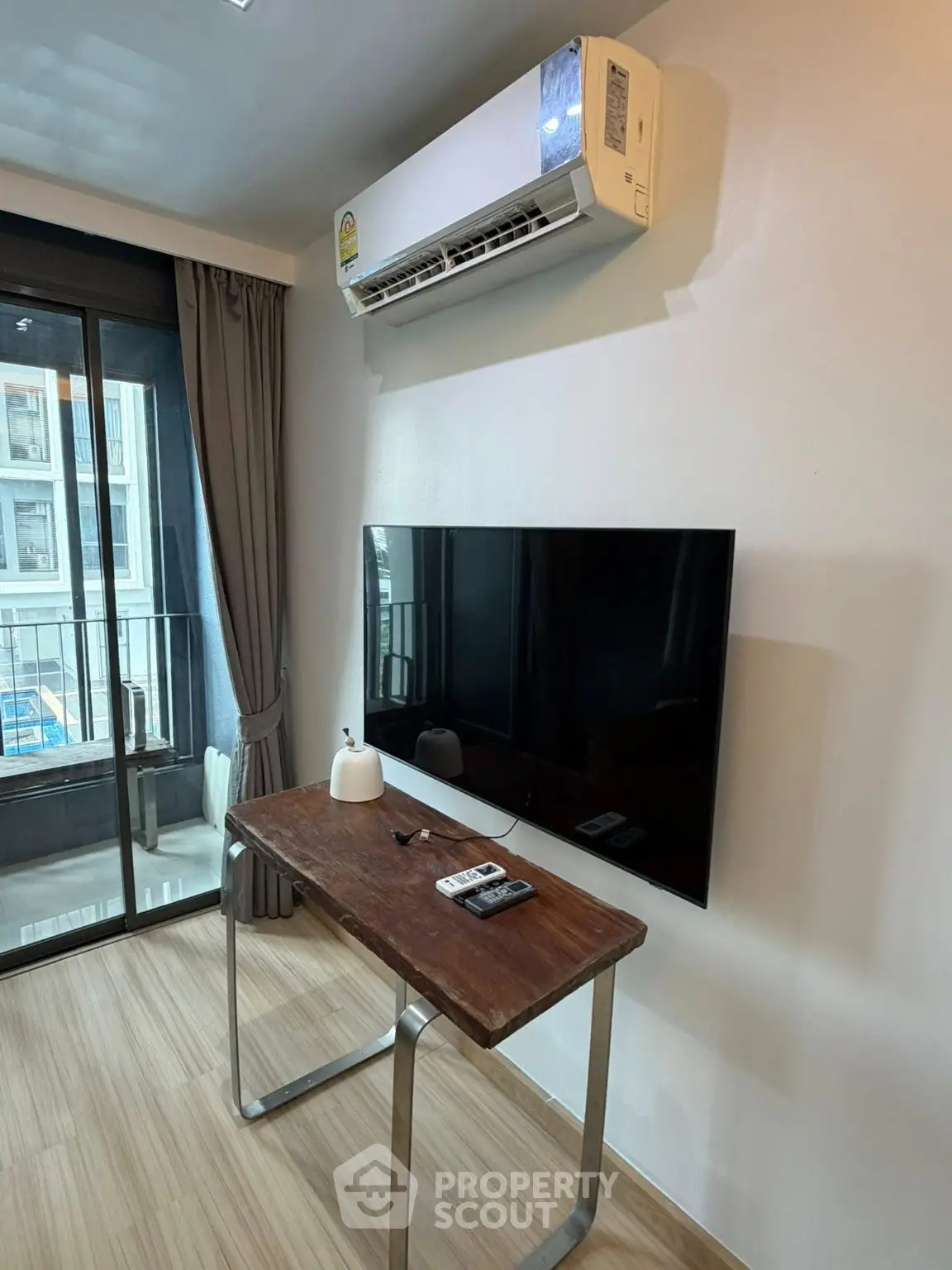 Modern living room with air conditioning and wall-mounted TV, featuring a sleek wooden desk and balcony access.