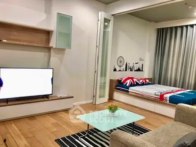 Modern living room with stylish decor and cozy bedroom area, featuring a sleek TV setup and wooden flooring.