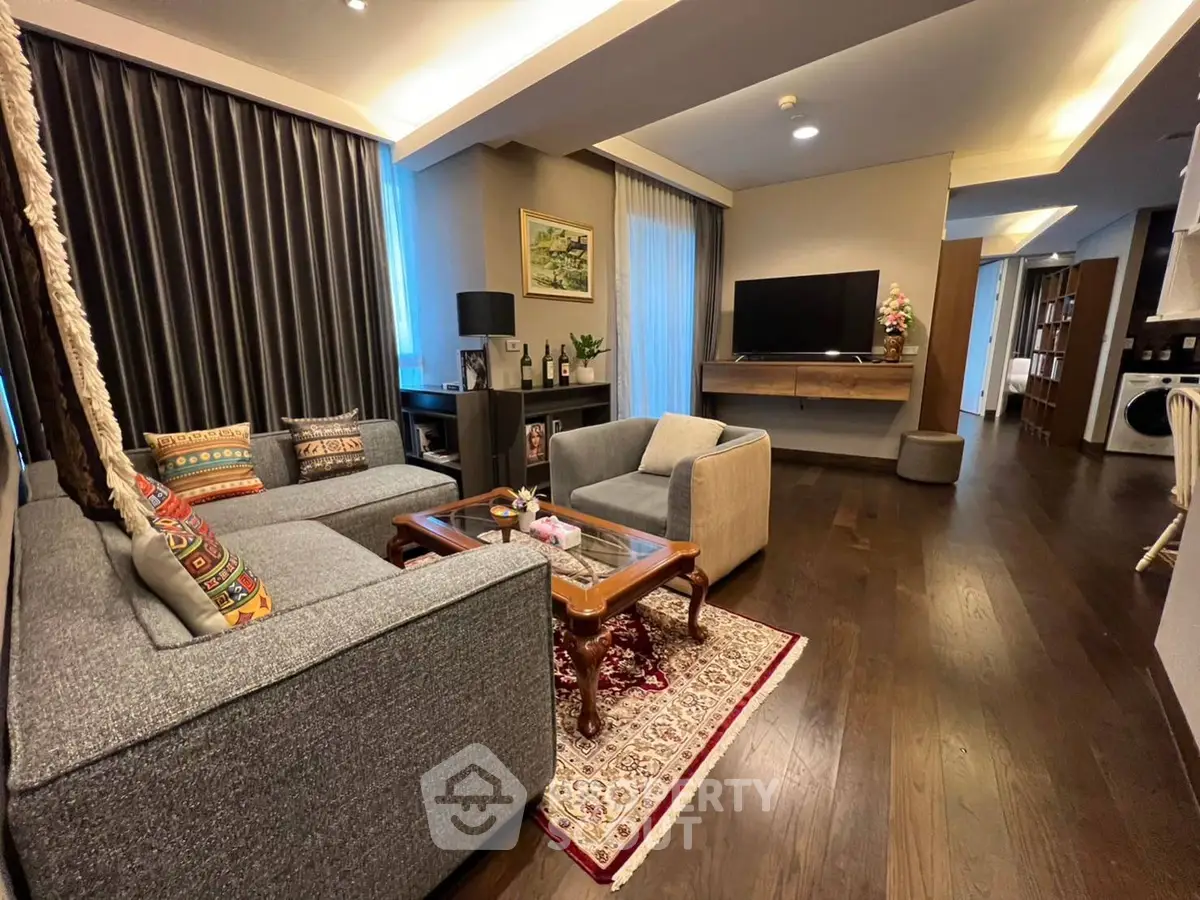 Spacious living room with elegant hardwood flooring, plush sofas, and modern entertainment unit, seamlessly connecting to an open-plan kitchen area.