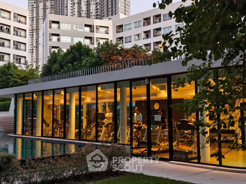Modern gym with glass walls overlooking a serene pool in a luxury residential complex.