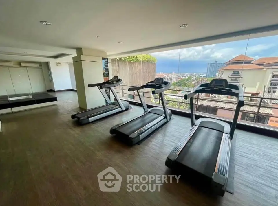 Modern gym with treadmills and panoramic city view in luxury apartment building.