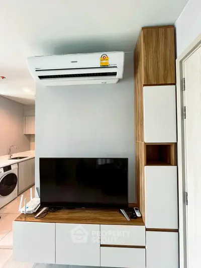Modern living room with sleek TV unit and air conditioning, featuring a compact kitchen area.