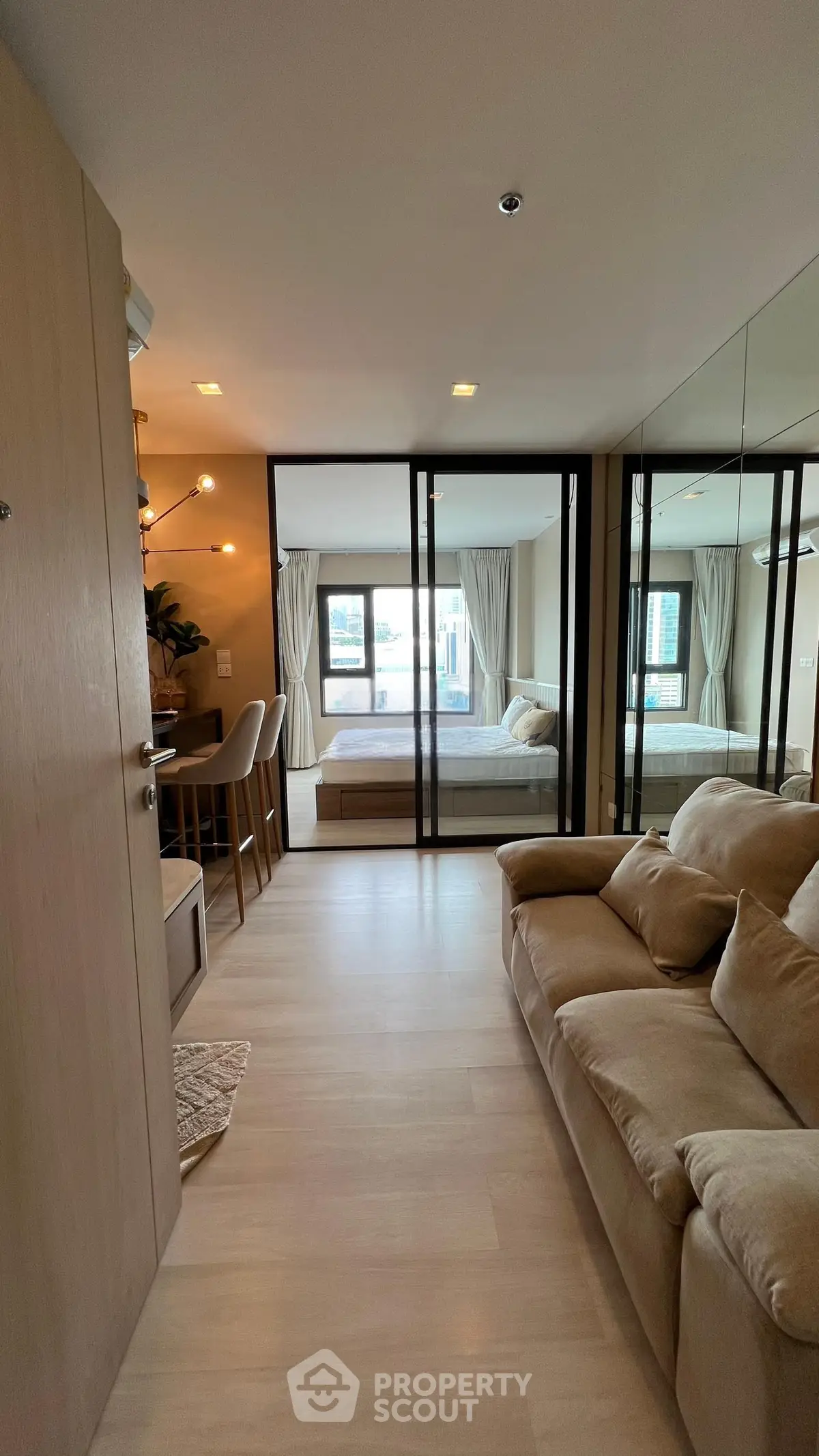 Modern open-plan living room with cozy sofa and mirrored walls leading to a stylish bedroom.