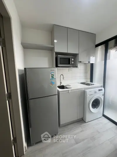 Modern compact kitchen with sleek appliances and washing machine in a stylish apartment.
