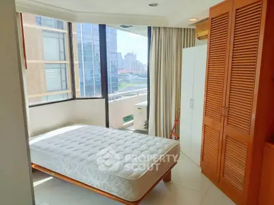 Bright bedroom with large windows and city view, featuring a comfortable bed and ample storage space.