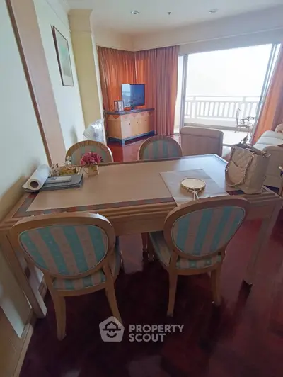 Elegant dining area with wooden table and chairs, adjacent to cozy living room with balcony view.