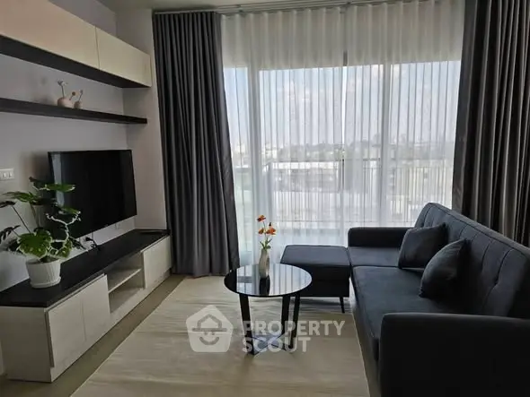 Modern living room with sleek furniture and large window offering natural light and city view.