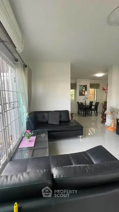 Spacious living room with modern black leather sofas and dining area in open layout.