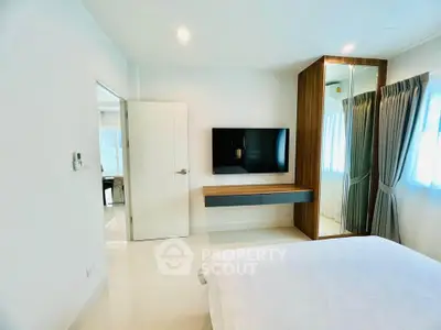 Modern bedroom with wall-mounted TV and mirrored wardrobe in bright apartment.