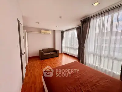 Spacious bedroom with large windows and wooden flooring, featuring a cozy sofa and modern decor.