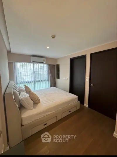 Modern bedroom with large window and city view, featuring a comfortable bed and sleek wooden flooring.