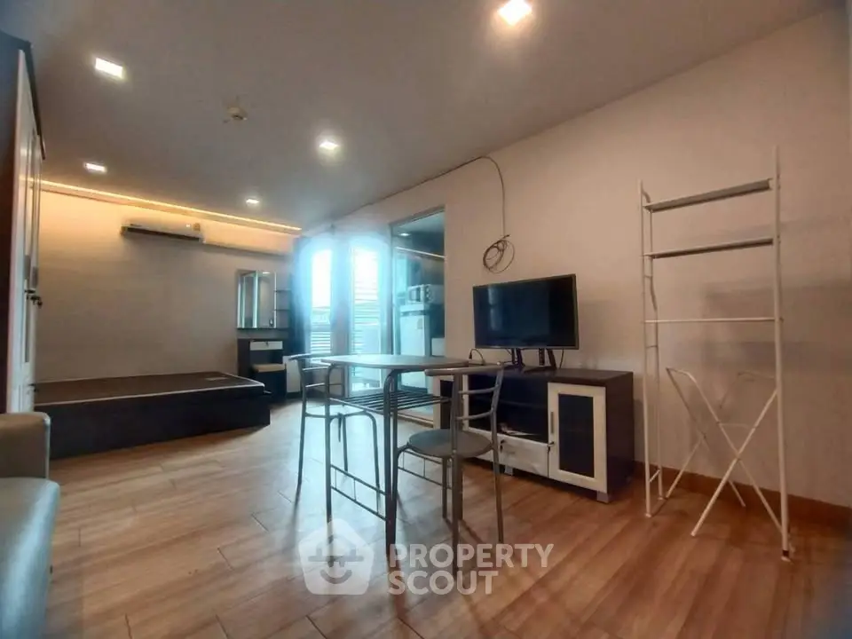 Modern living room with sleek furniture and wooden flooring, featuring a TV and dining area.