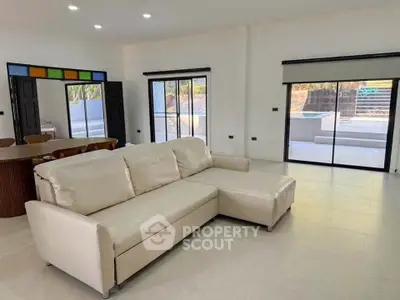Spacious modern living room with large sofa and sliding glass doors leading to outdoor pool area.