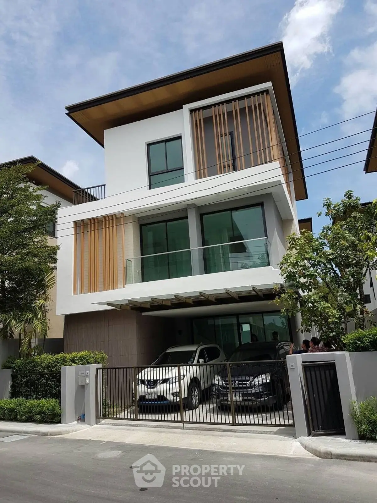 Modern three-story house with sleek design and spacious carport in a suburban neighborhood.