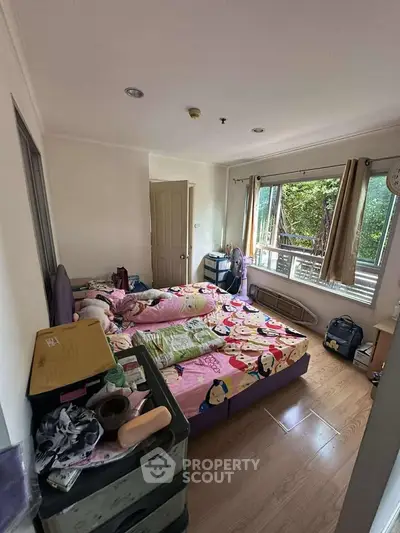 Cozy bedroom with large window and wooden flooring, featuring colorful bedding and ample natural light.