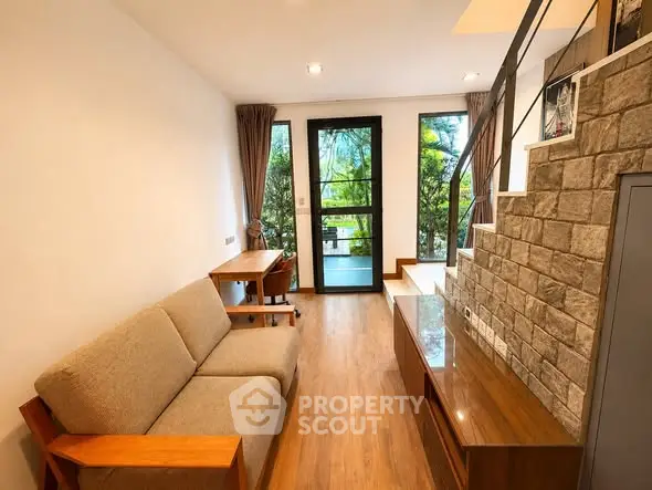 Modern living room with stylish staircase and natural light, featuring cozy sofa and wooden flooring.