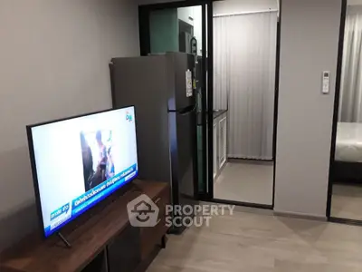 Modern apartment interior with sleek kitchen and cozy living area featuring a flat-screen TV and refrigerator.