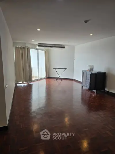 Spacious living room with wooden flooring and large windows for natural light.