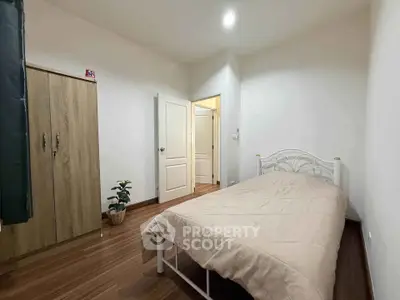Cozy bedroom with wooden flooring and minimalist decor, featuring a single bed and wardrobe.