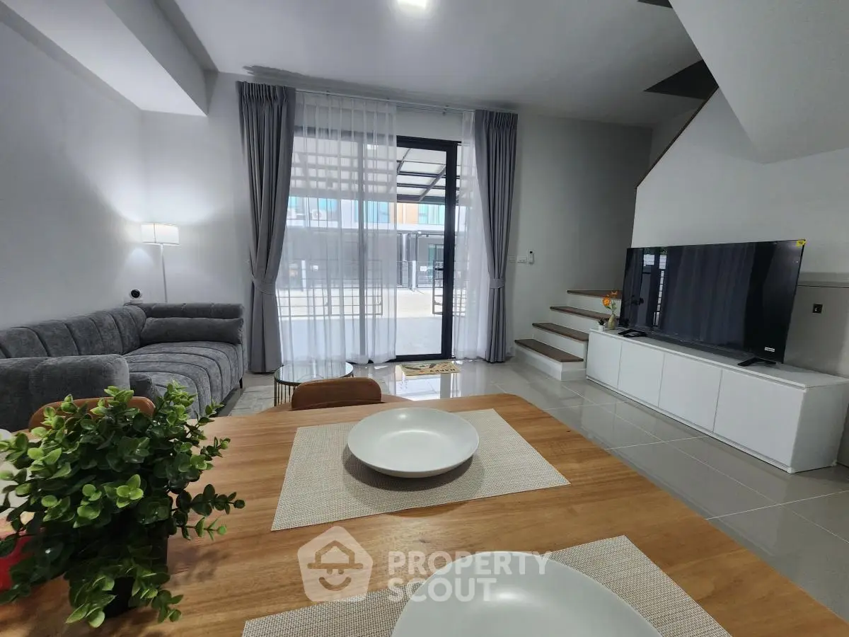 Modern living room with stylish decor and natural light, featuring a cozy sofa and a flat-screen TV.