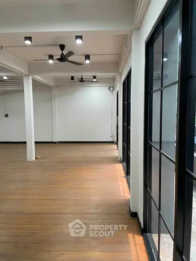 Spacious open-plan interior with wooden flooring and large windows, ideal for versatile use.