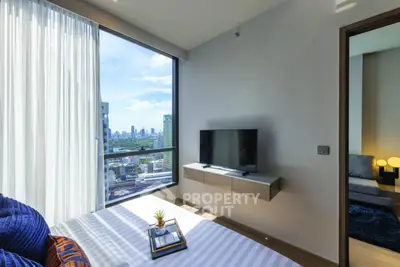 Modern bedroom with city view, featuring a wall-mounted TV and stylish decor.