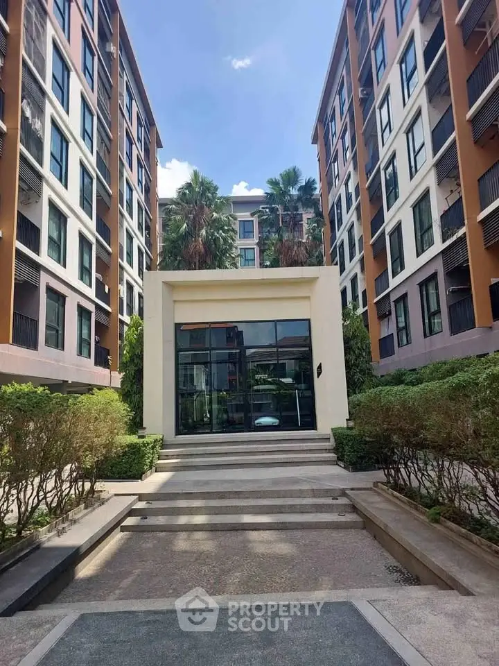 Modern apartment building entrance with lush greenery and contemporary design.
