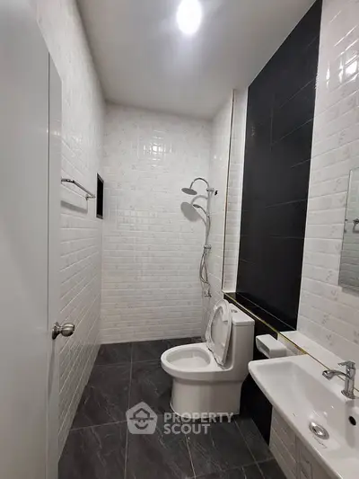 Modern bathroom with sleek black and white tiles, featuring a shower and contemporary fixtures.