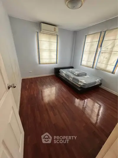 Spacious bedroom with wooden flooring and natural light, featuring a comfortable bed and air conditioning.