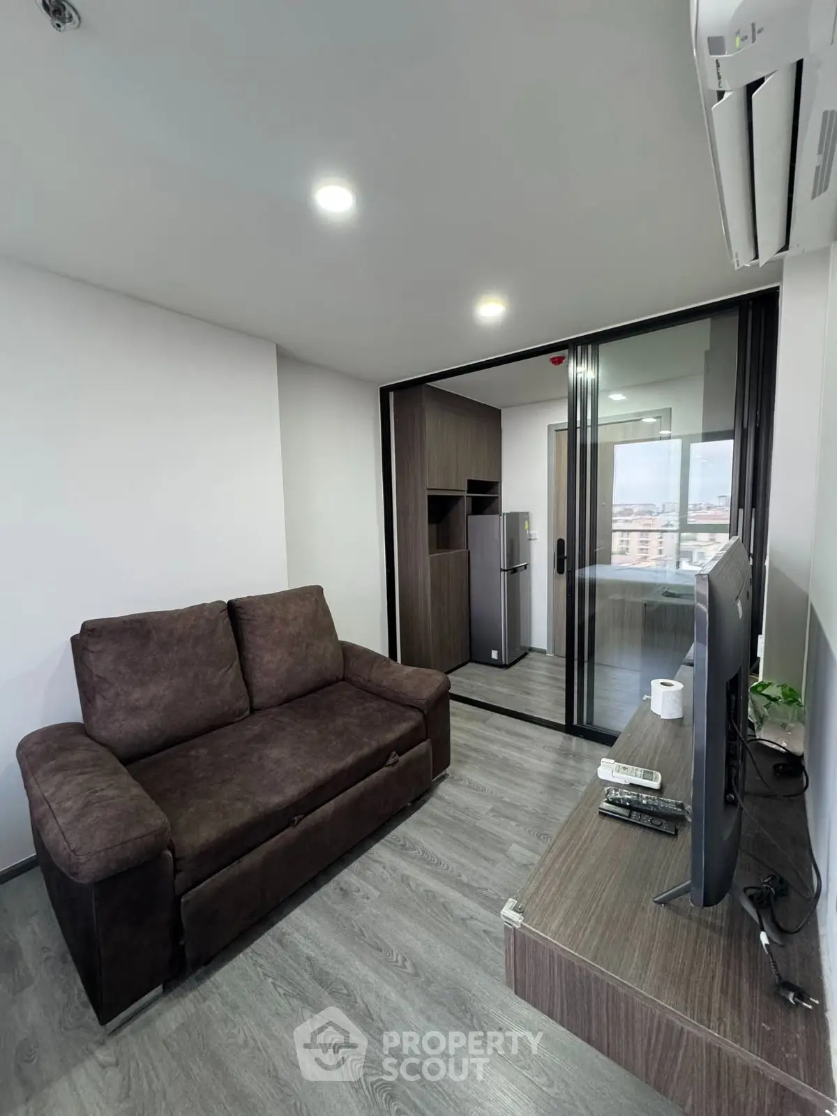 Modern living room with sleek design and balcony view, featuring a comfortable sofa and flat-screen TV.