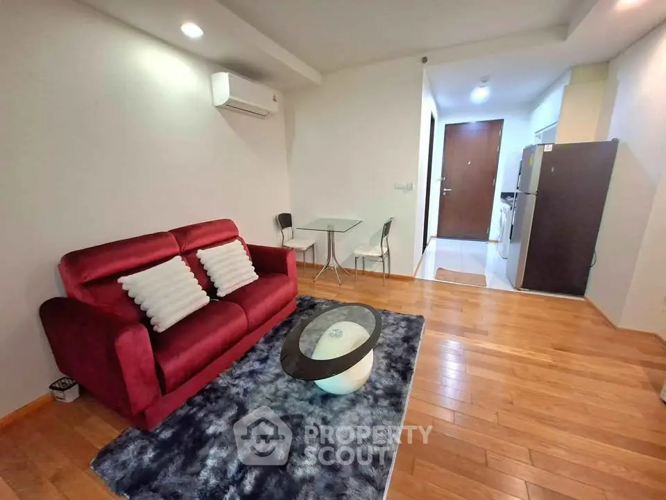 Modern living room with red sofa, wooden flooring, and compact dining area in open layout apartment.