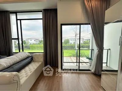 Spacious living room with large windows and balcony overlooking lush greenery.