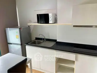 Modern kitchen with sleek black countertop, stainless steel sink, fridge, and microwave.